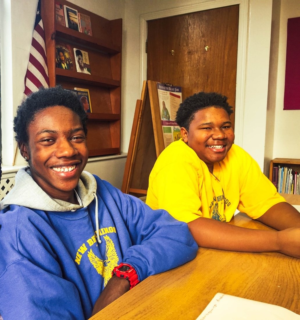 Two students in academy sweatshirts smiling at a classroom table