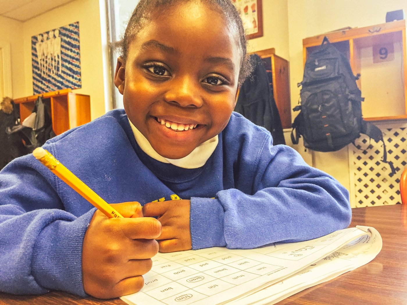 A young student smiling while writing at her desk